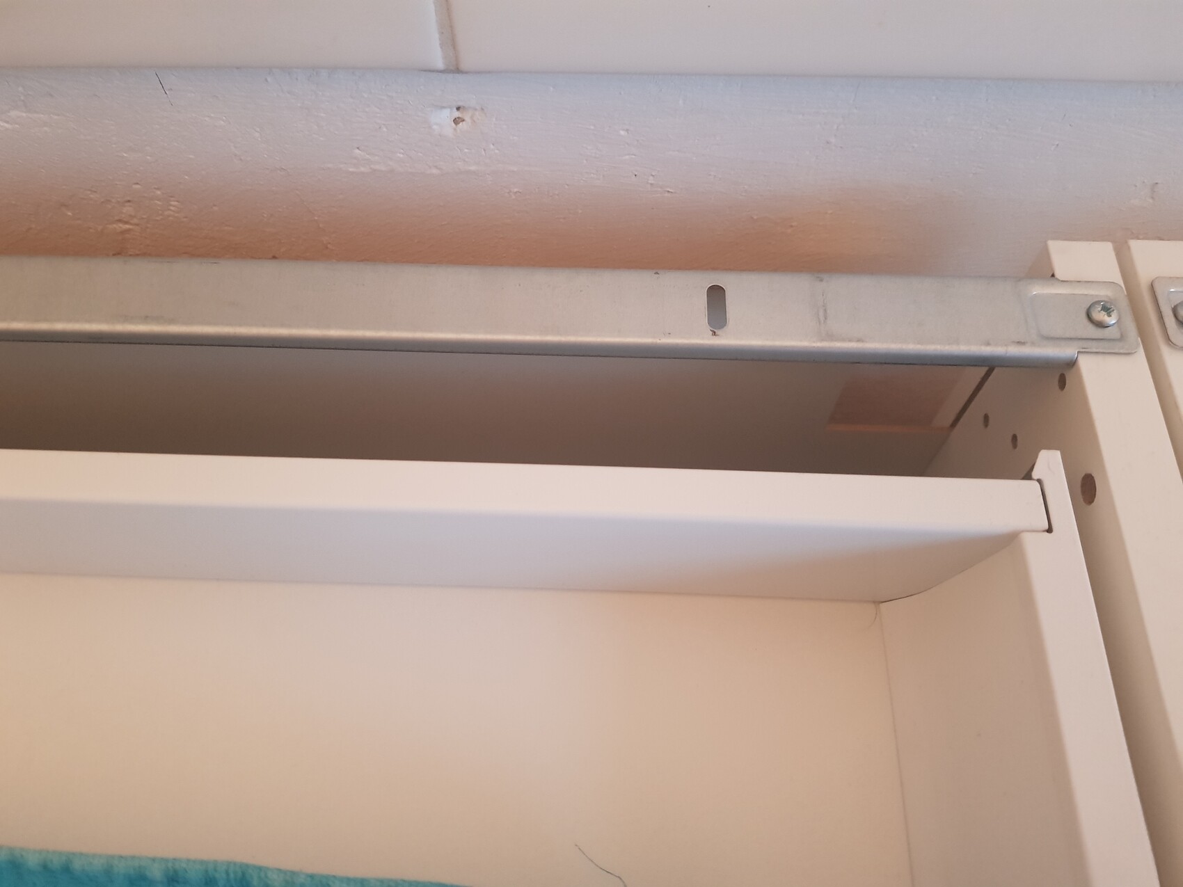 Weiße Schubladenführung aus Metall im offenen Schrank sichtbar.
