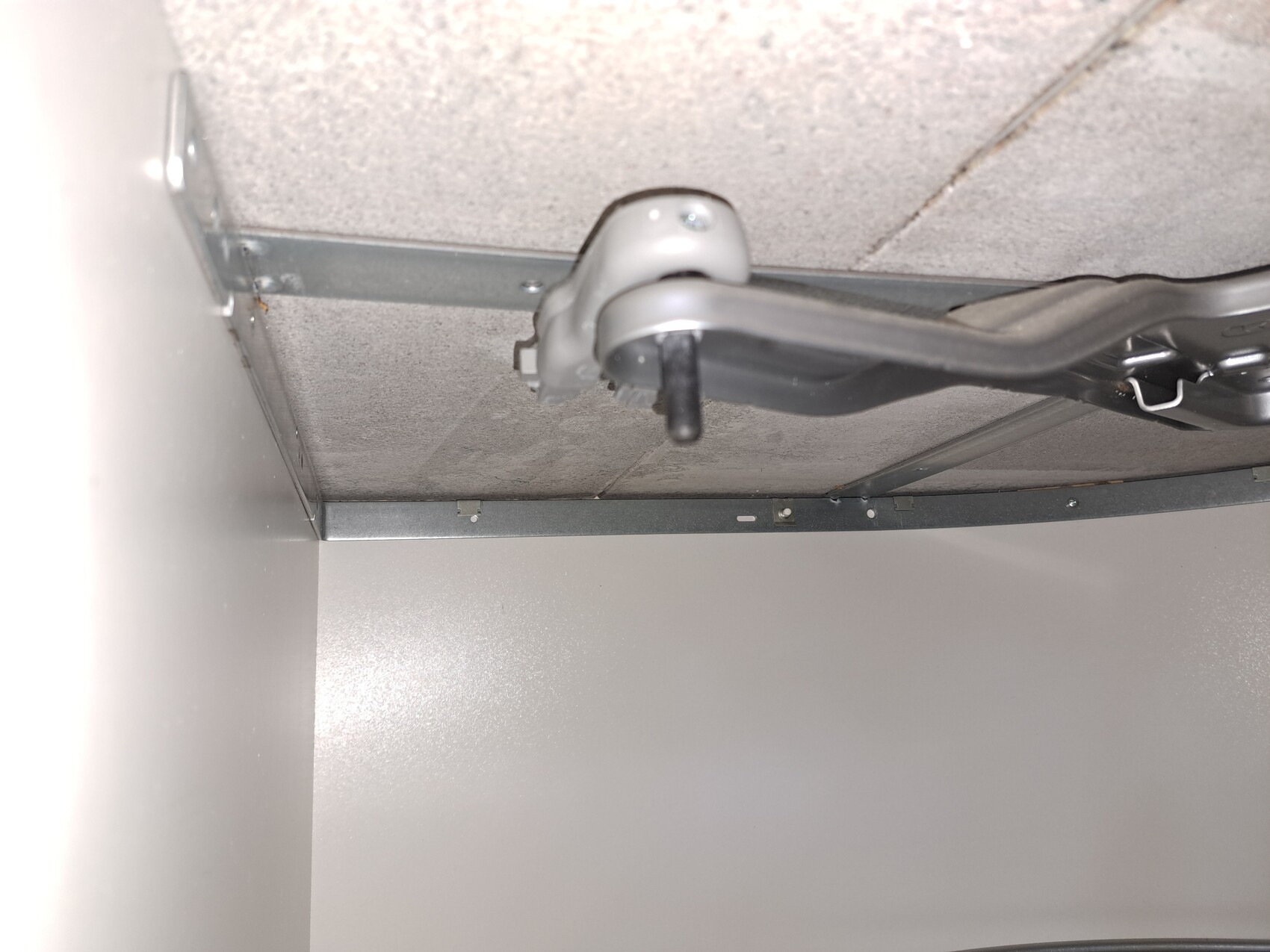 Unterseite eines Schranks mit Metallführung, grauem Beschlag und schwarzem Hebel.