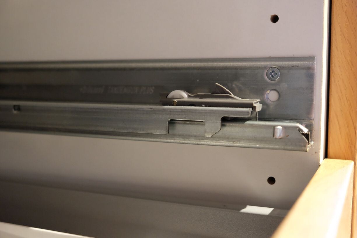 Nahaufnahme einer Metallschubladenschiene mit Schrauben, daneben ein kleines Spielzeugauto