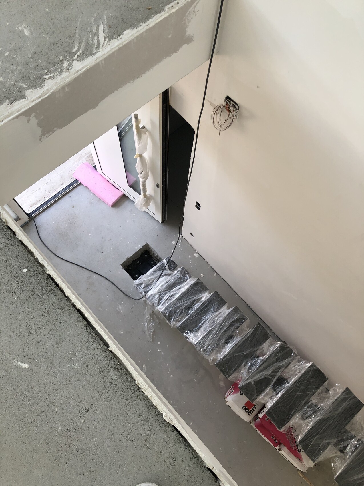 Innen-Baustelle: verpackte Treppe, Kabelgewirr an der Wand, Türöffnung nach draußen.