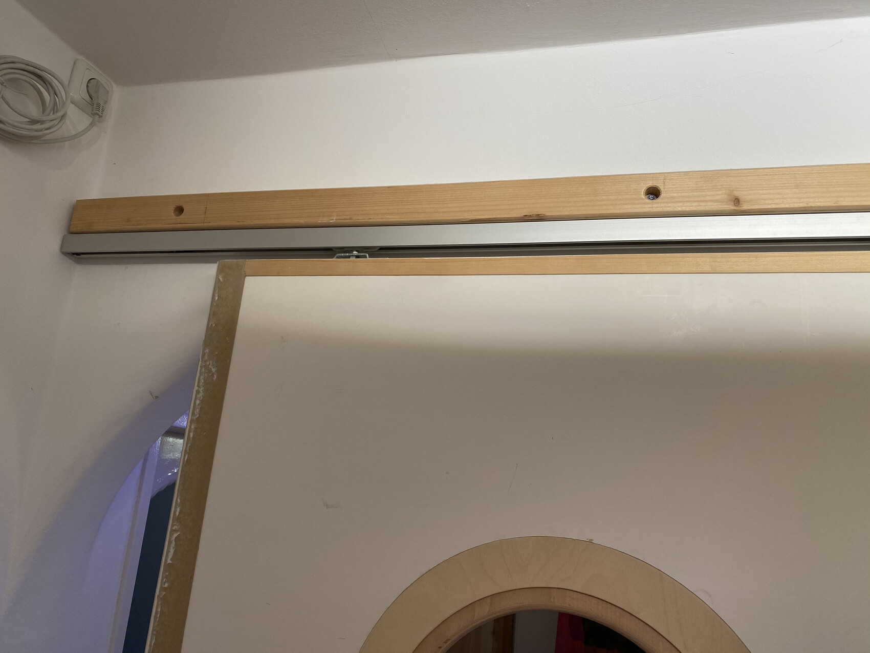 Innenraum mit Holzbalken-Struktur an der Decke, Metall-Schiebetür-Schiene, runder Türrahmen unten rechts.