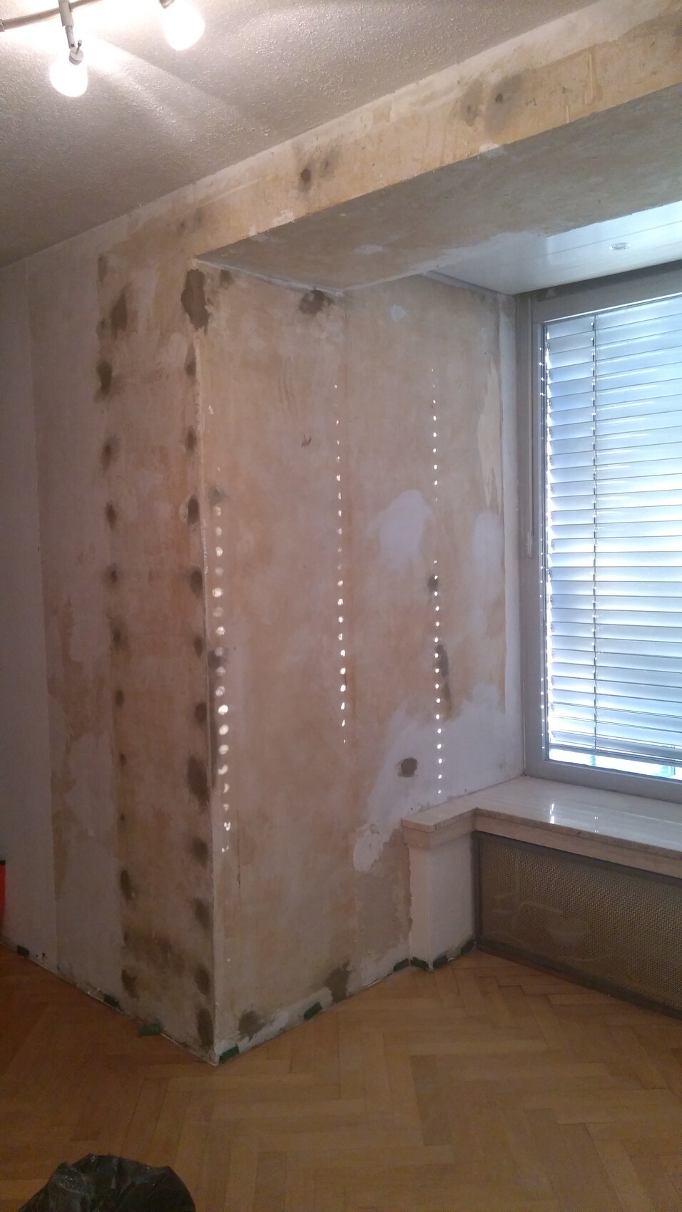 Freigelegte Wand bei Renovierung mit vielen Bohrlöchern; Fenster mit Rollladen, Holzboden.