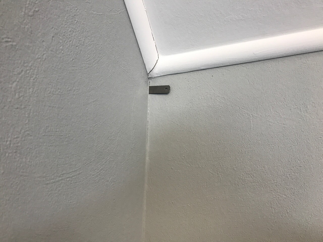 Kleine metallische Halterung in einer Innenwand-Ecke zwischen Decke und Wand