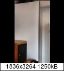 Heller Innenraum-Ecke mit weißer Wand und kleinem Holzschrank links.