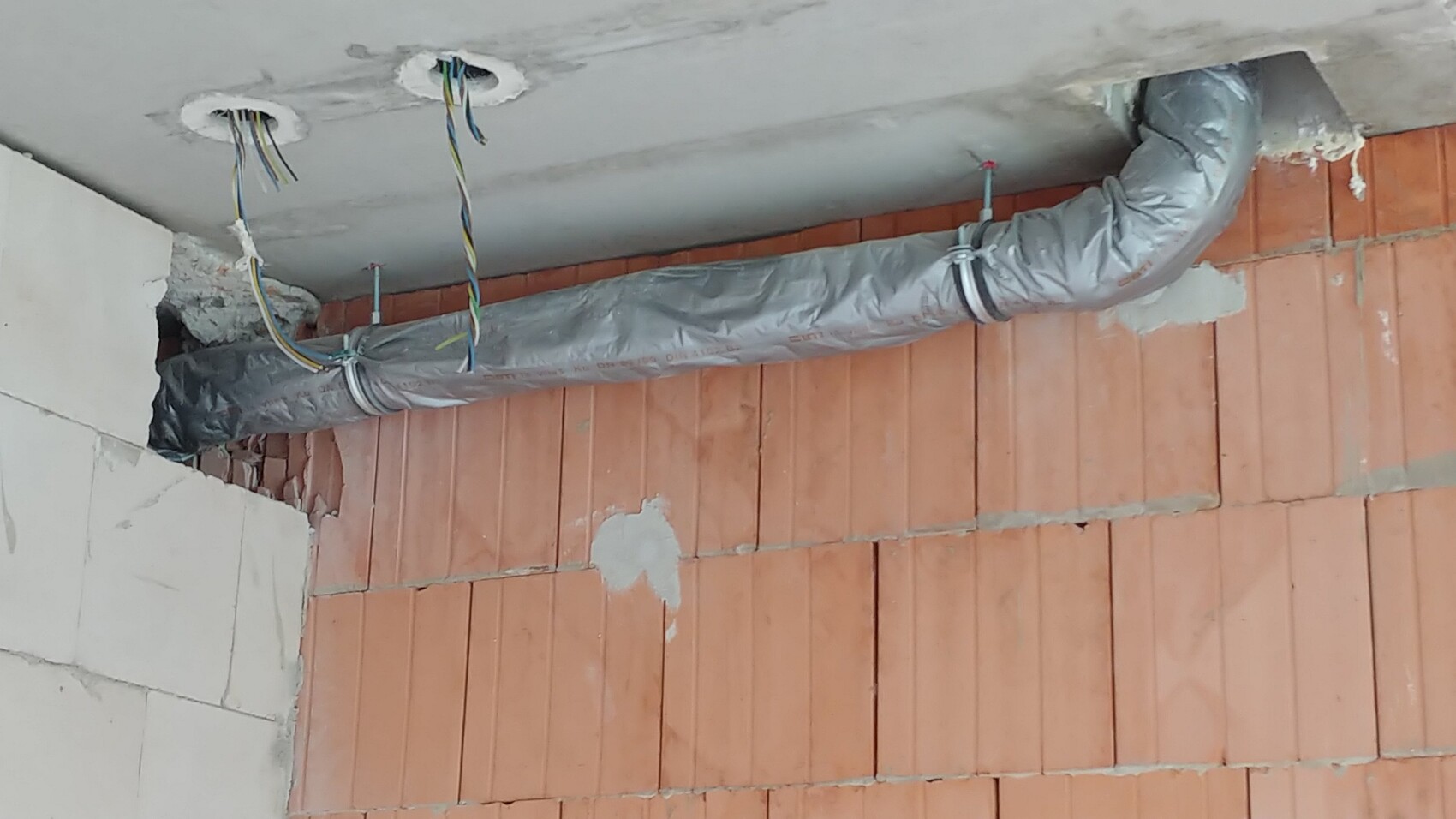 Baustellenszene mit Installationsrohren, Verkabelung und roter Ziegelwand