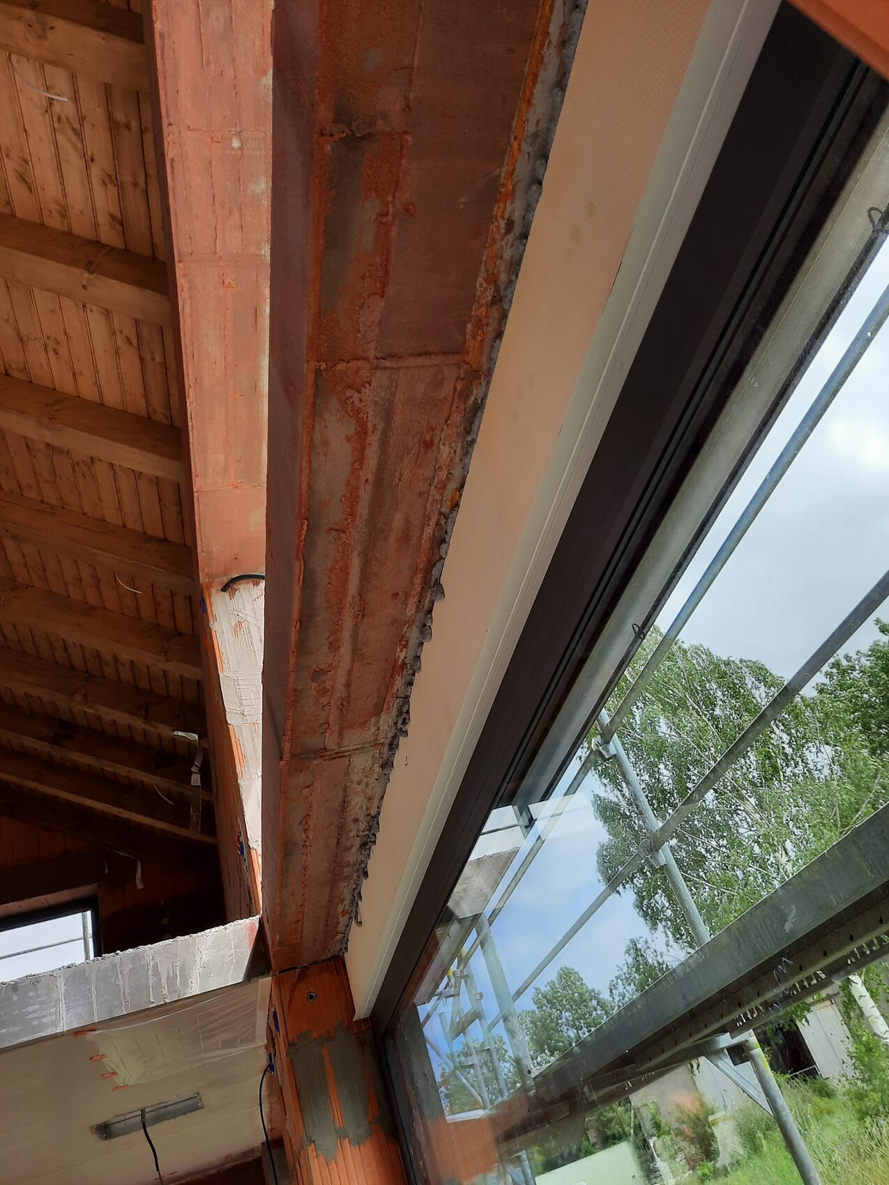 Innenraum einer Baustelle: Holzdecke, Backsteinstütze, großes Fenster mit Gerüst außen.