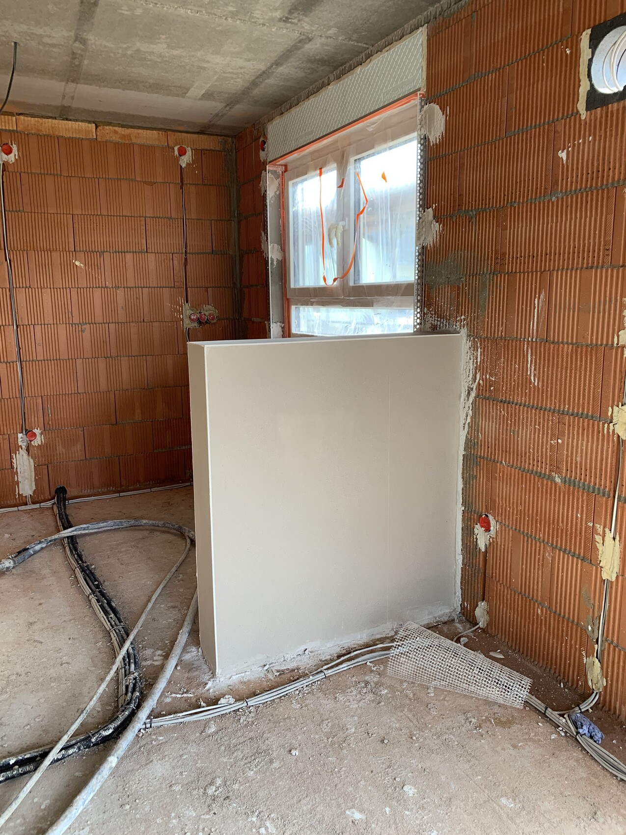 Rohbau: rote Ziegelwände, Fenster mit Plastikfolie, freistehende weiße Wandplatte, Kabel am Boden.