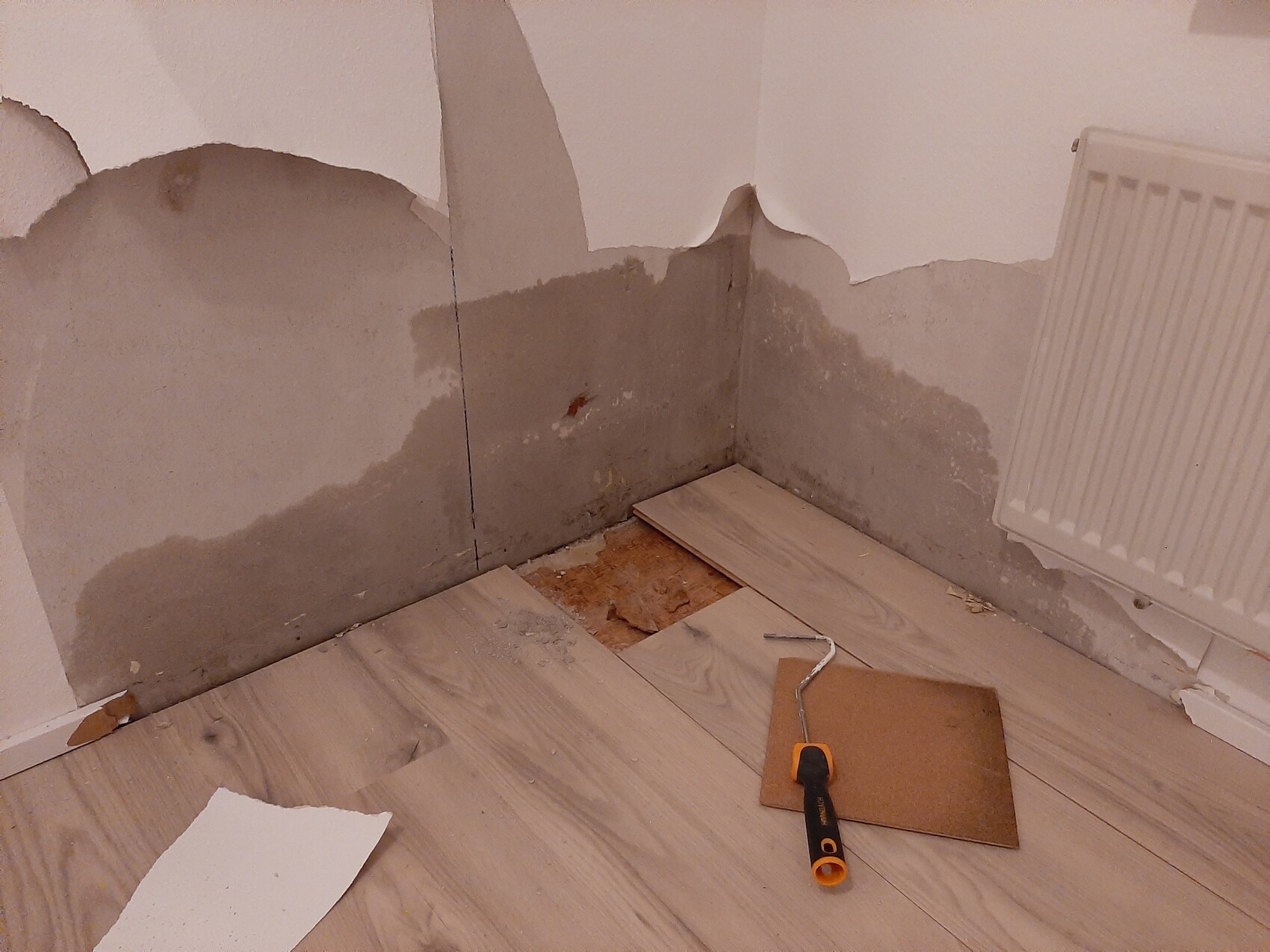 Renovierungswinkel mit beschädigter Wand, freiliegtem Putz, Laminatboden und Werkzeug.