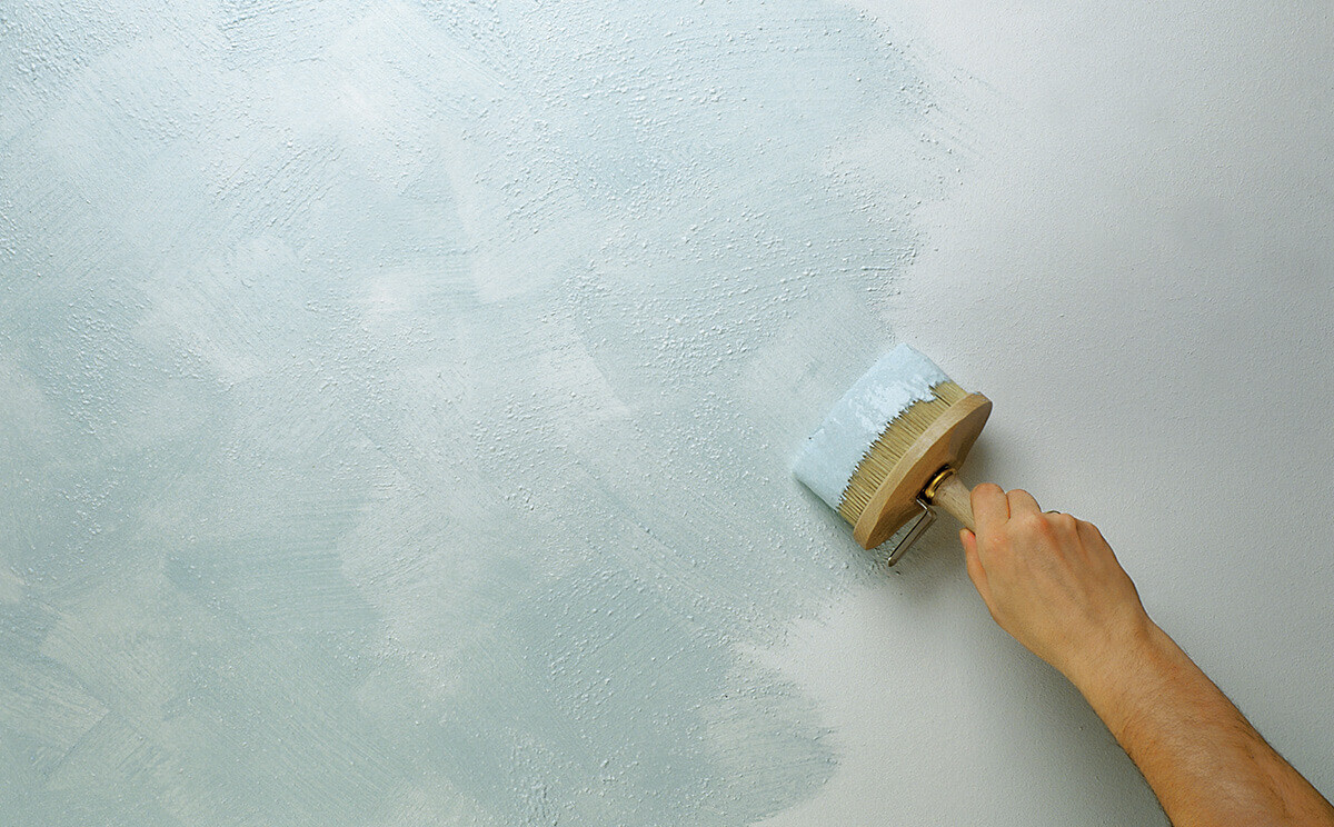Hand mit Farbrolle streicht hellblaue Farbe auf eine Wand.