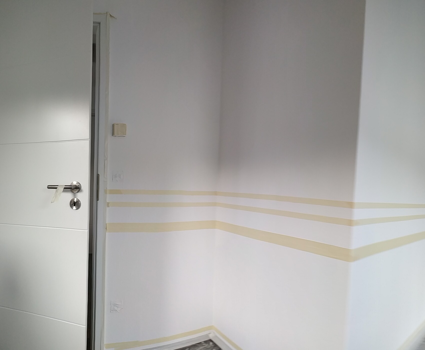 Weiße Innenwand mit Tür, Wände für Malerarbeiten abgeklebt, Malerbandlinien sichtbar