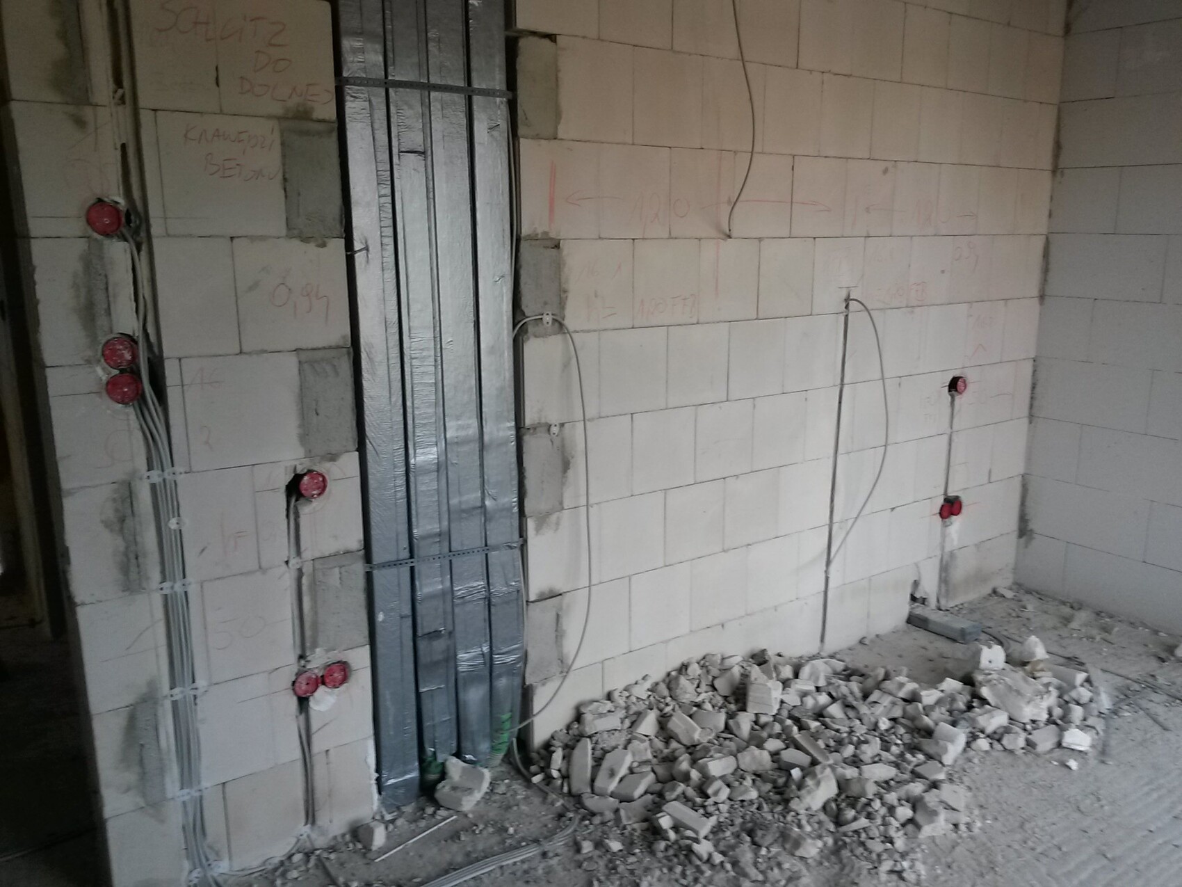 Baustelle: Wand aus Steinblöcken, sichtbare Elektroverkabelung, rote Steckdosen, Geröll am Boden.