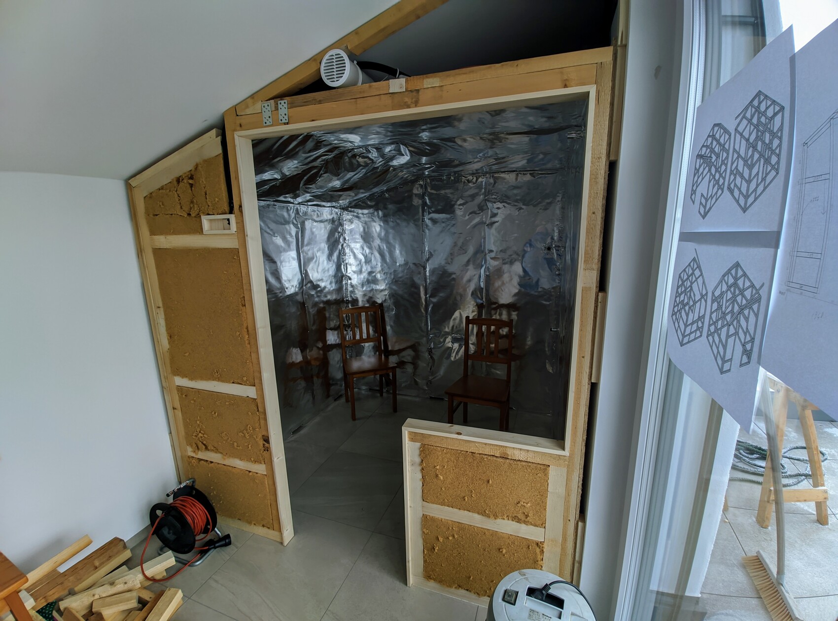Provisorischer Raum mit Alu-Folie an den Wänden, zwei Holzstühle im Innenraum