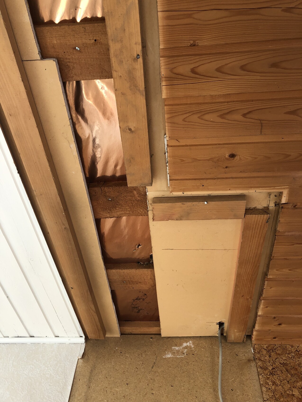 Freigelegte Wandkonstruktion mit Holzlatten, Dämmung und Kabel am Boden.