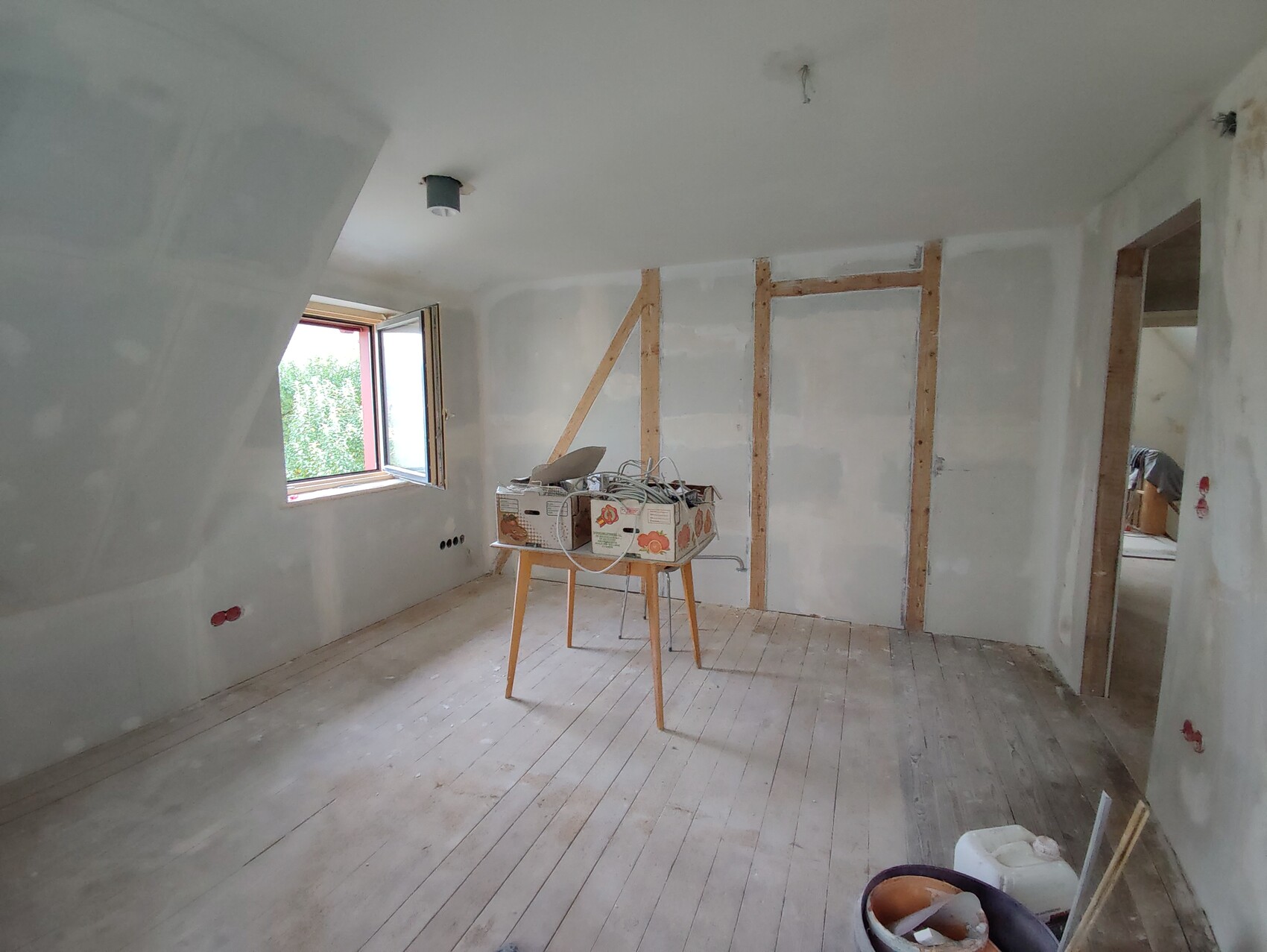 Unfertiger Renovierungsraum: sichtbare Holzrahmen, offenes Fenster, Werkbank mit Boxen.