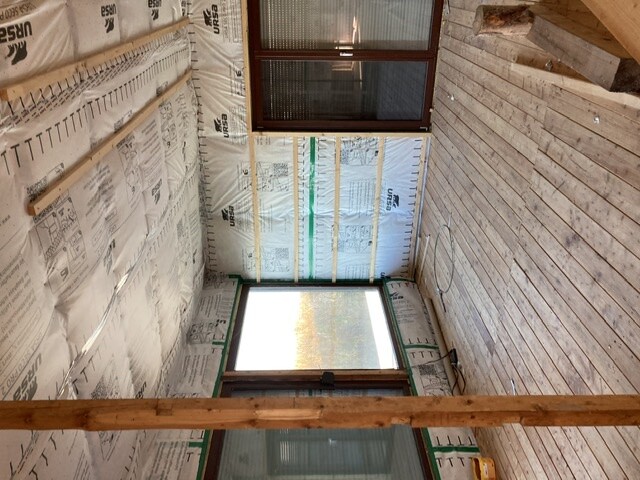 Innenraum einer Baustelle: Dämmfolie an den Wänden, sichtbare Holzlatten, Fensterfronten.