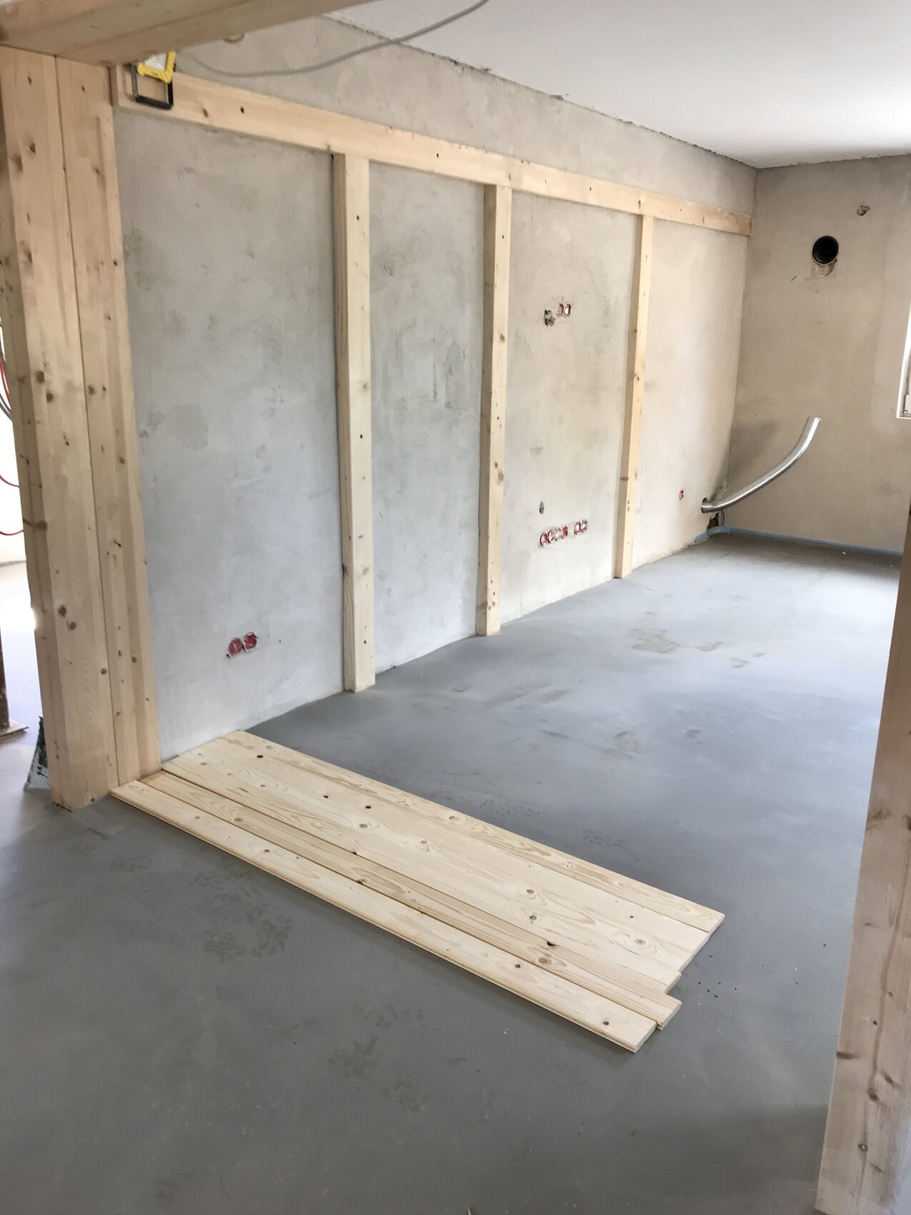 Baustelle: freigelegte Holzständerwand, Rohbau mit Kabelanschlüssen und Holzbretter auf dem Boden.