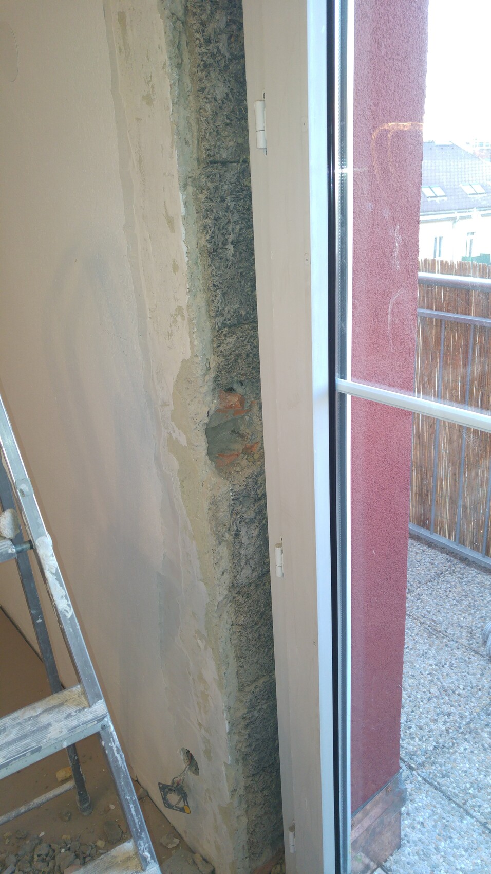 Innenraum Baustelle: unverputzte Wand mit Dämmung neben Fenster, Leiter steht bereit.