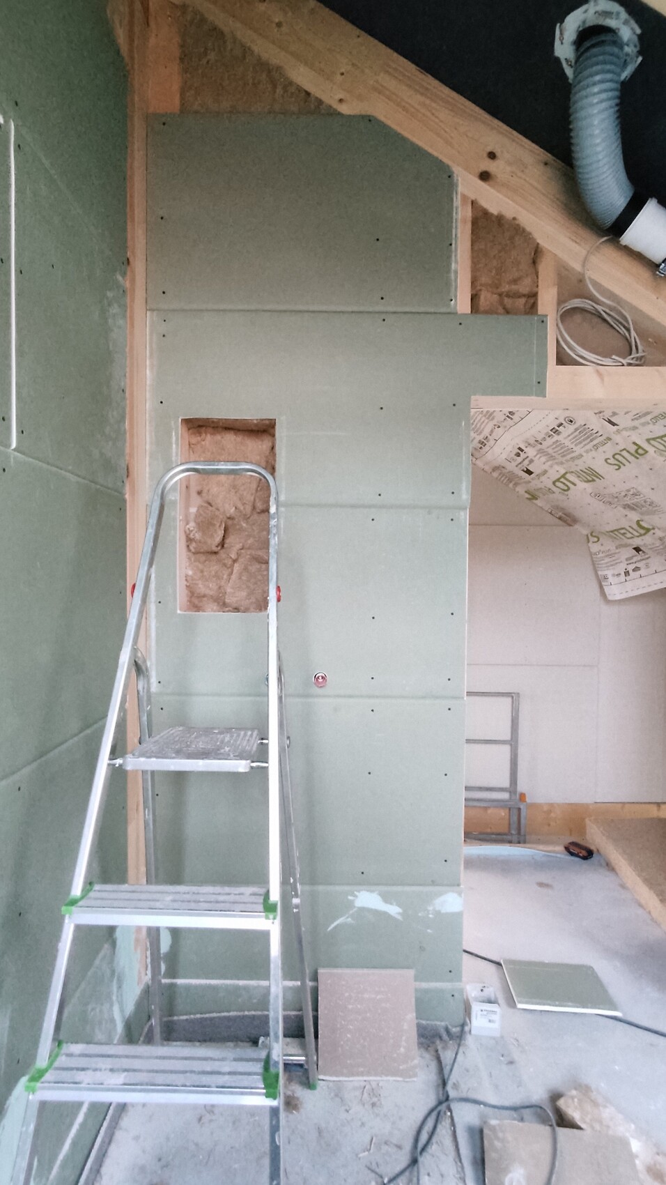 Baustelle: Leiter vor grünem Trockenbau, offener Wandausschnitt, Dämmmaterial dahinter.