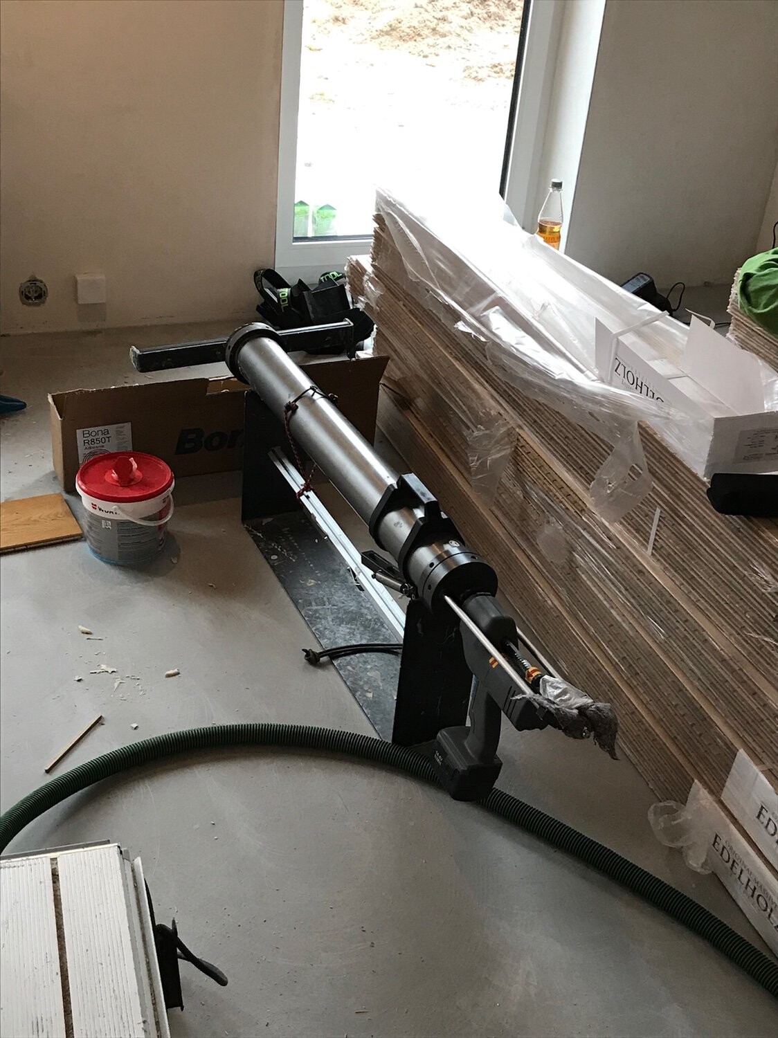 Innenraum-Bau: langes Metallwerkzeug auf Stativ, gestapelte Holzplatten, grüner Schlauch, Eimer und Kartons.