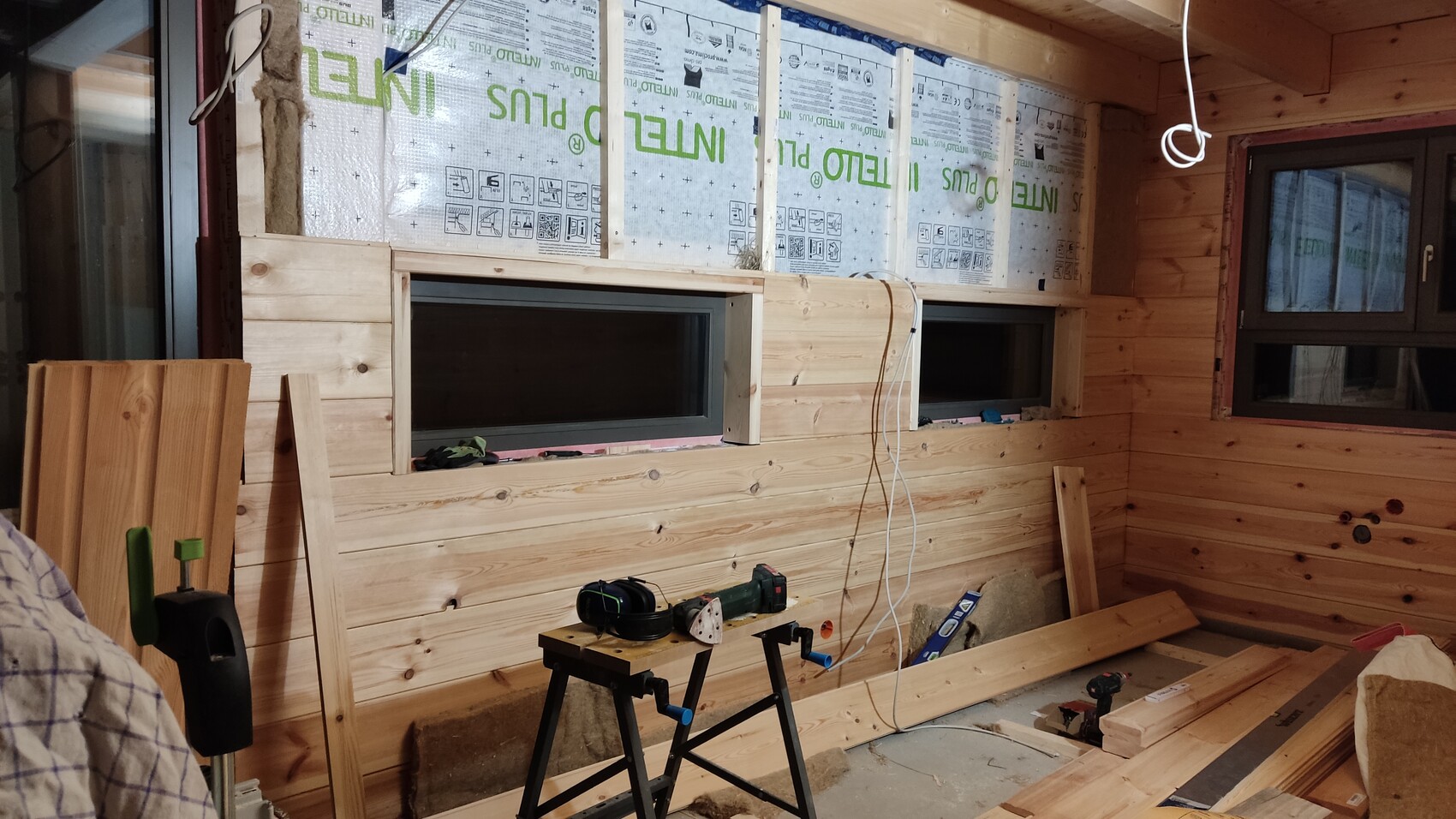 Innenraum einer Holzhütte im Bau: Holzverkleidung, zwei Fenster, Werkzeuge und Baustoffe.