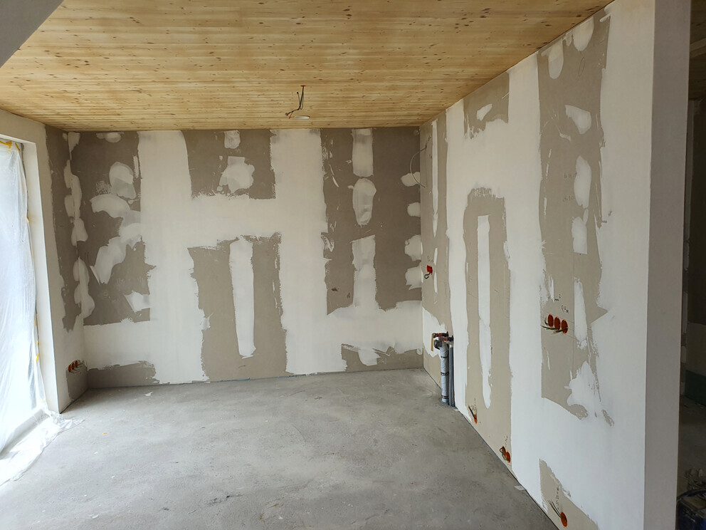 Unfertiger Innenraum mit Trockenbauwänden, Spachtelarbeiten, Holzdecke und Rohboden
