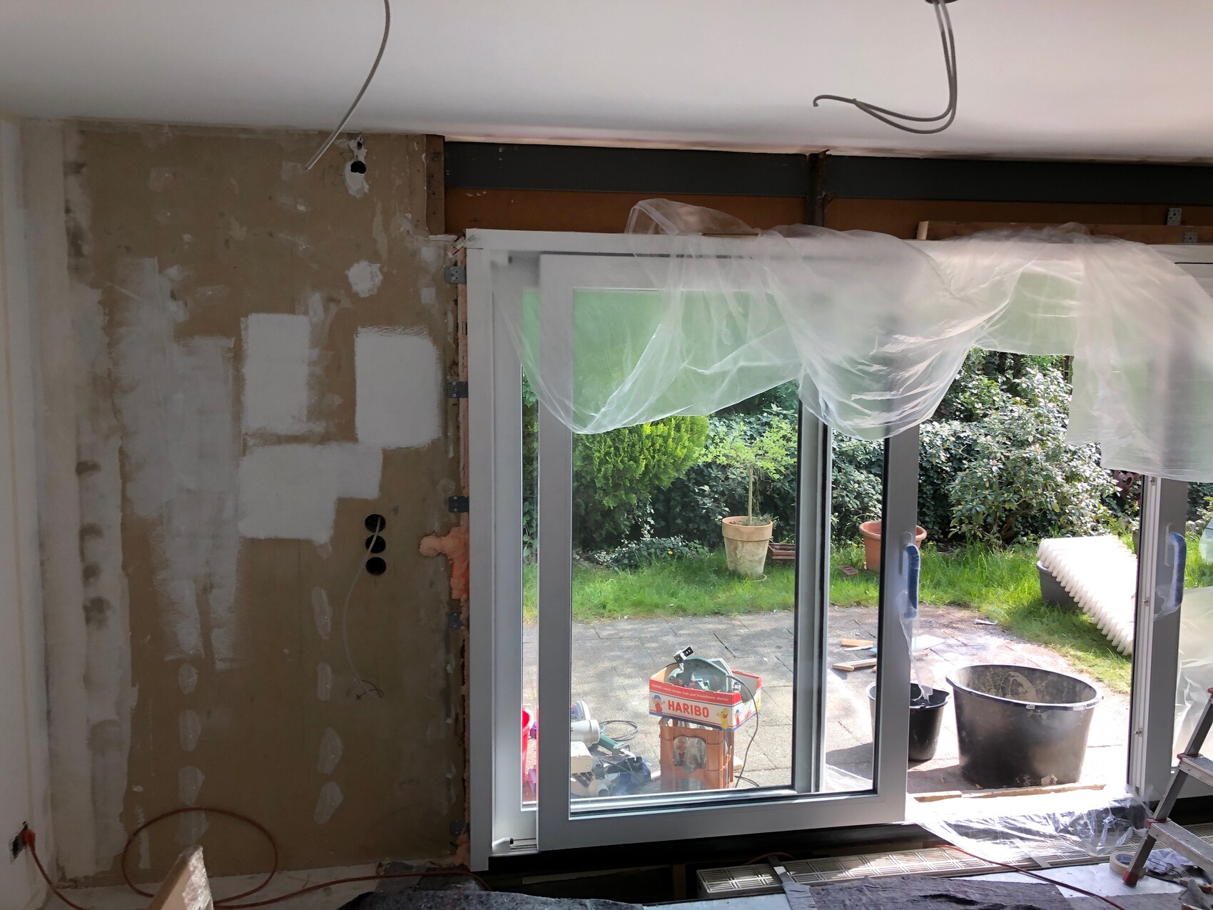 Renovierung: freigelegte Wand, Glas-Schiebetür zum Garten, Plastikfolie bedeckt.