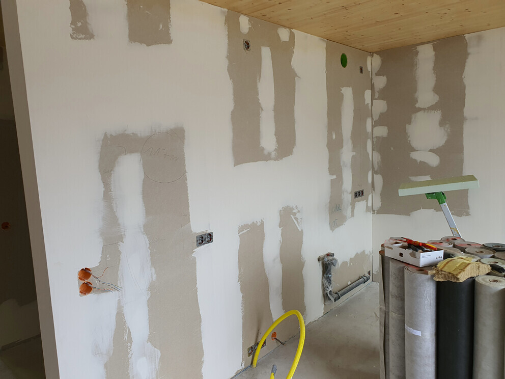 Unfertige Innenwand mit Trockenbau-Patches, Steckdosen und Bauwerkzeugen.