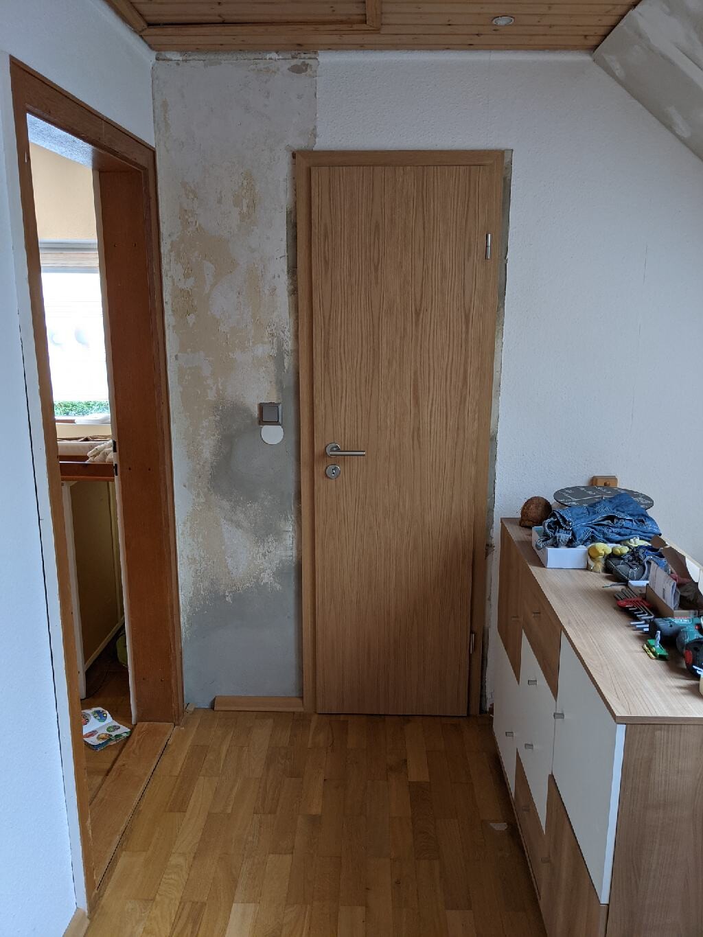 Flurraum mit Holztür, verputzte Wand und Kommode mit Werkzeugen.