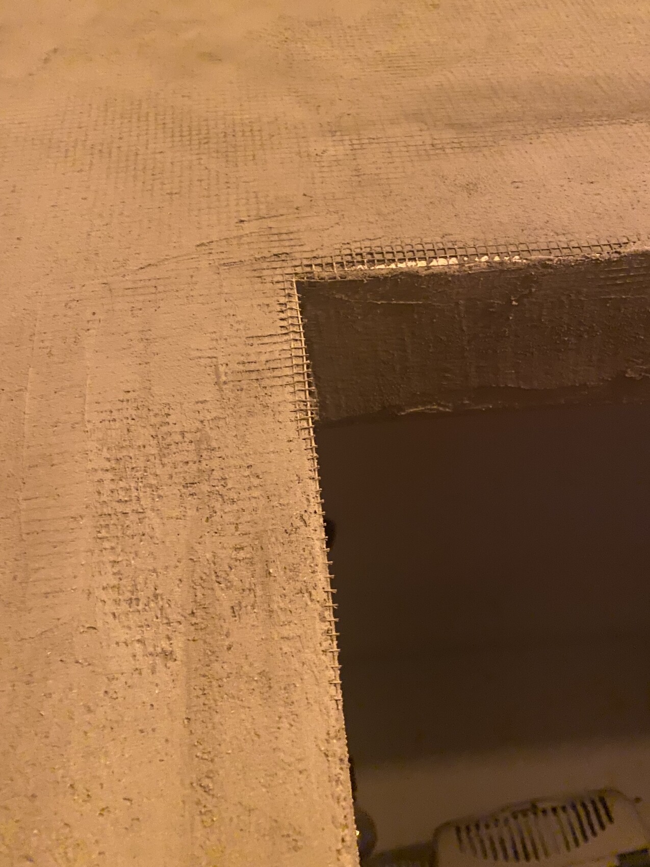 Rohbau-Szene im Innenbereich mit rauem Wandputz und Metall-Gitterkante an einer Aussparung