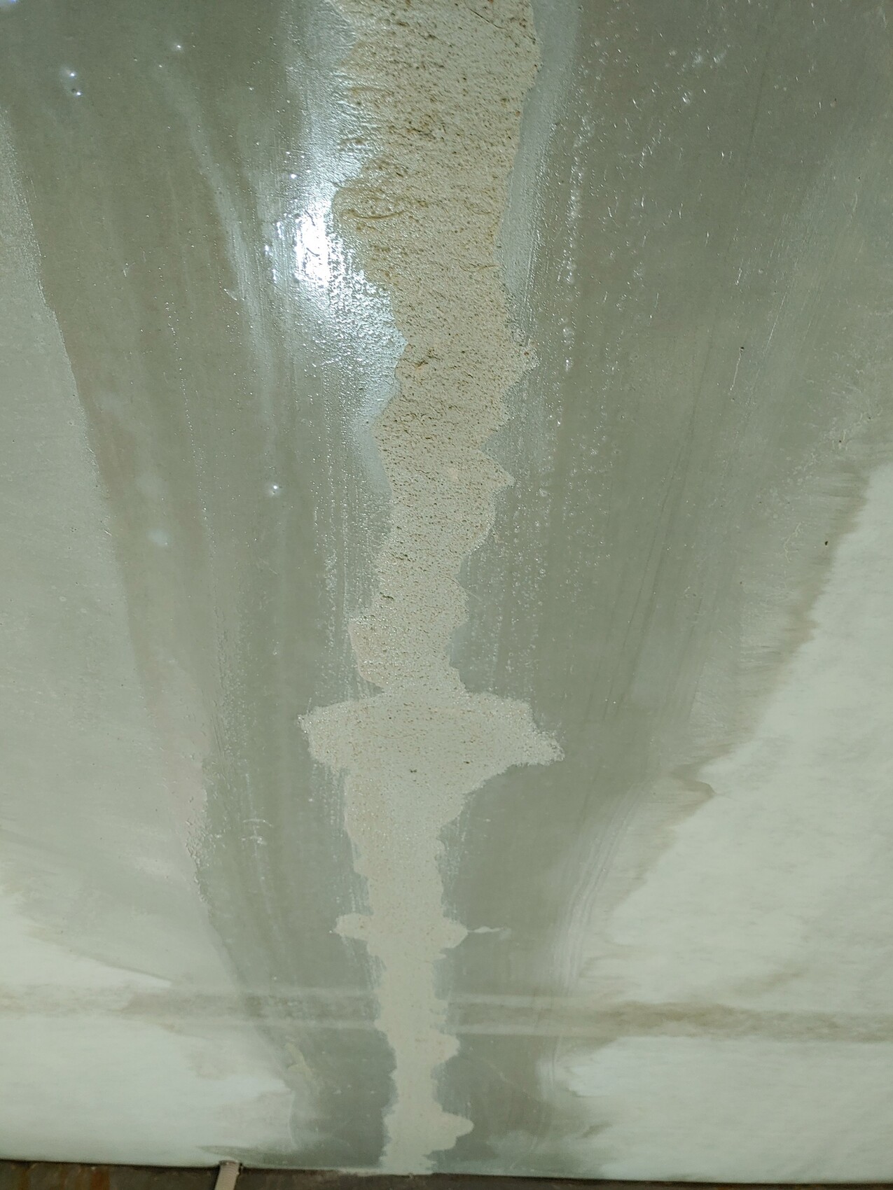 Vertikaler Wandriss mit cremefarbener Spachtelmasse auf grünlich-grauer Oberfläche.