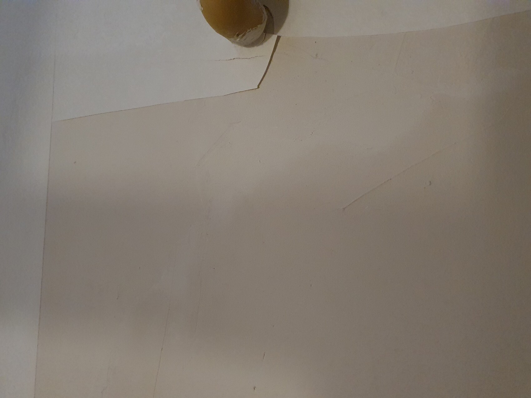 Unfertige Innenwand mit Putzrissen und Rohr in der Ecke.
