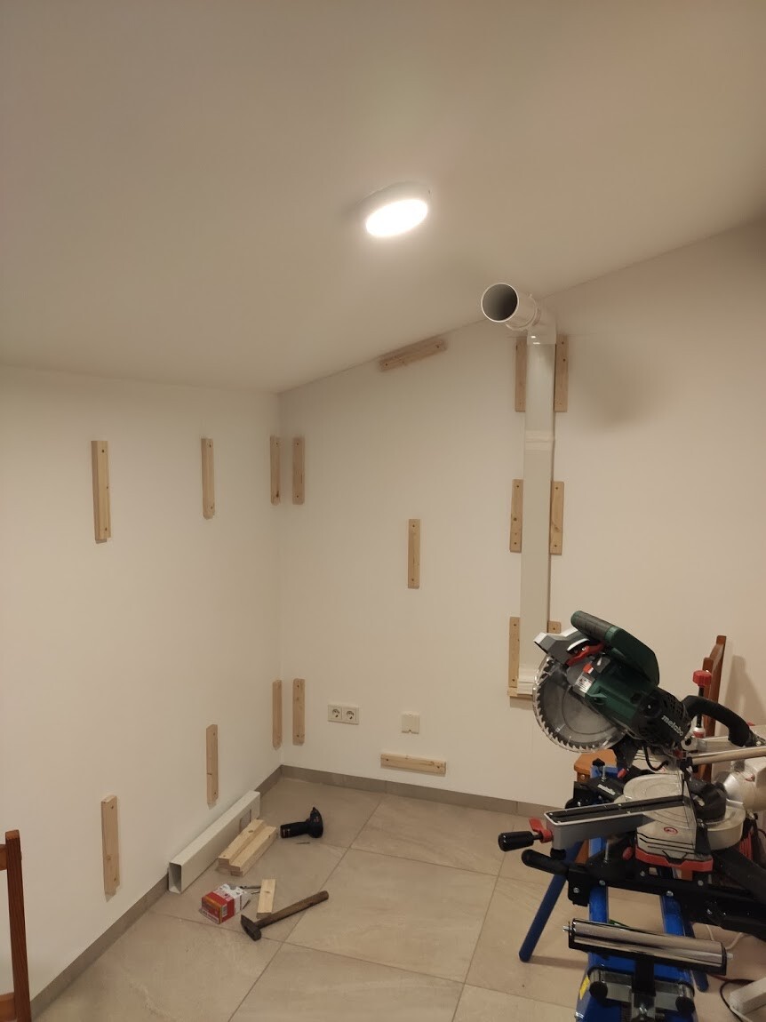 Werkstatt im Bau: Kreissäge auf Stativ, Holzbretter an Wänden, Baumaterialien auf dem Boden.