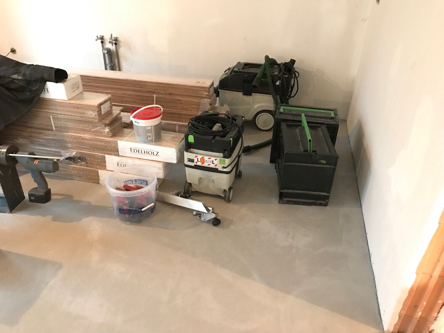 Renovierungsraum mit gestapelten Holzlatten, Eimer, Werkzeugkisten und Maschinen.