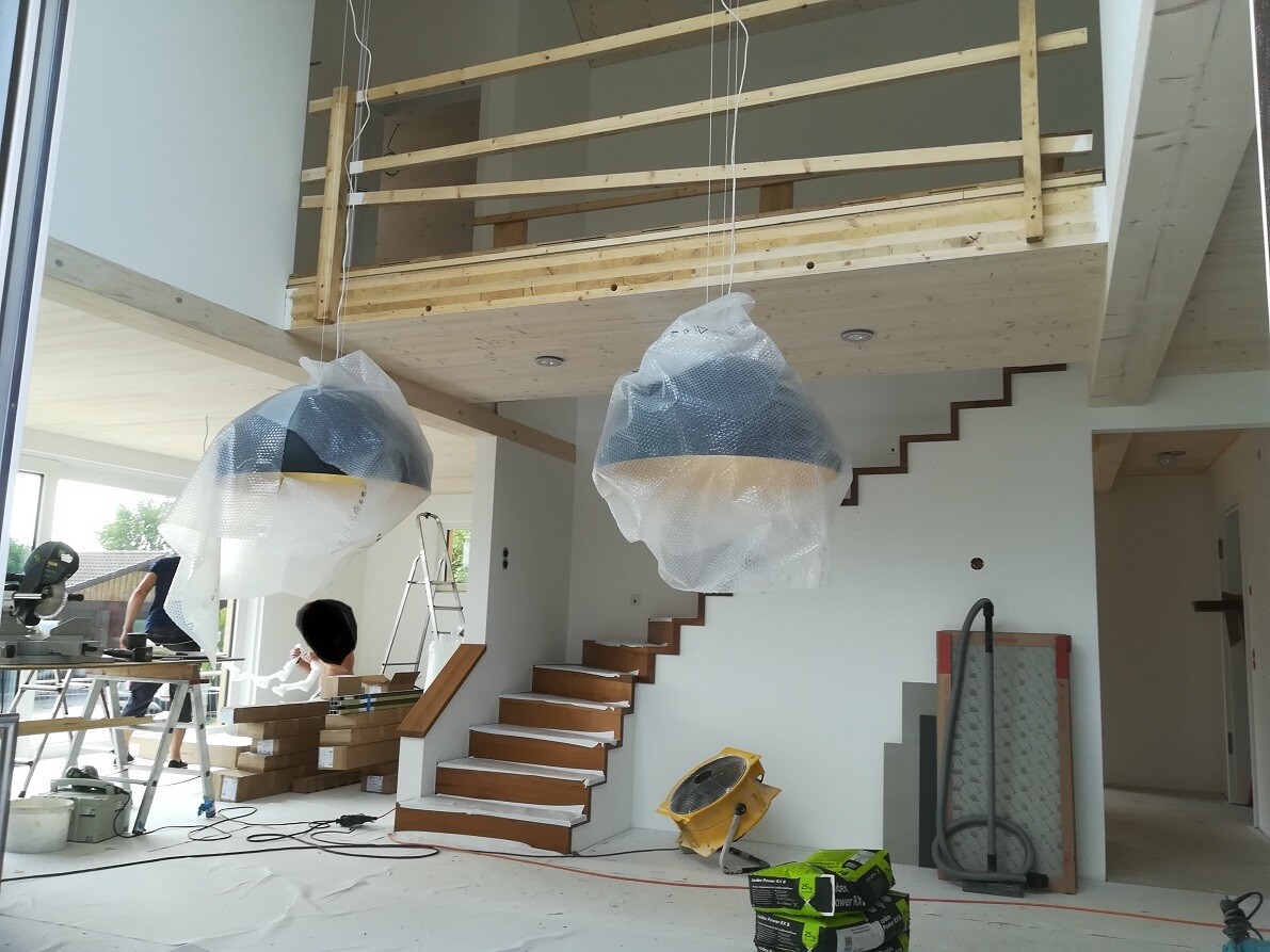 Innenansicht einer Baustelle: Hängende, eingewickelte Lampen, Holztreppe, Werkzeug.