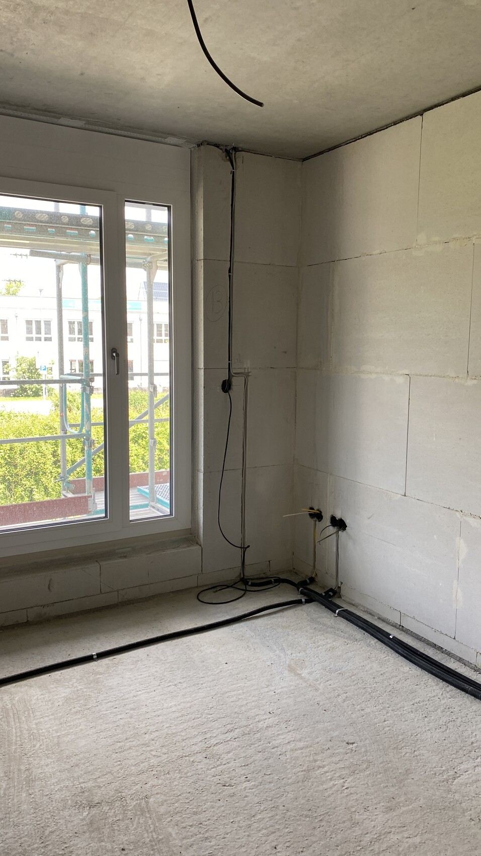 Unfertiger Innenraum auf Baustelle mit rohen Wänden, Fenster und Kabeln