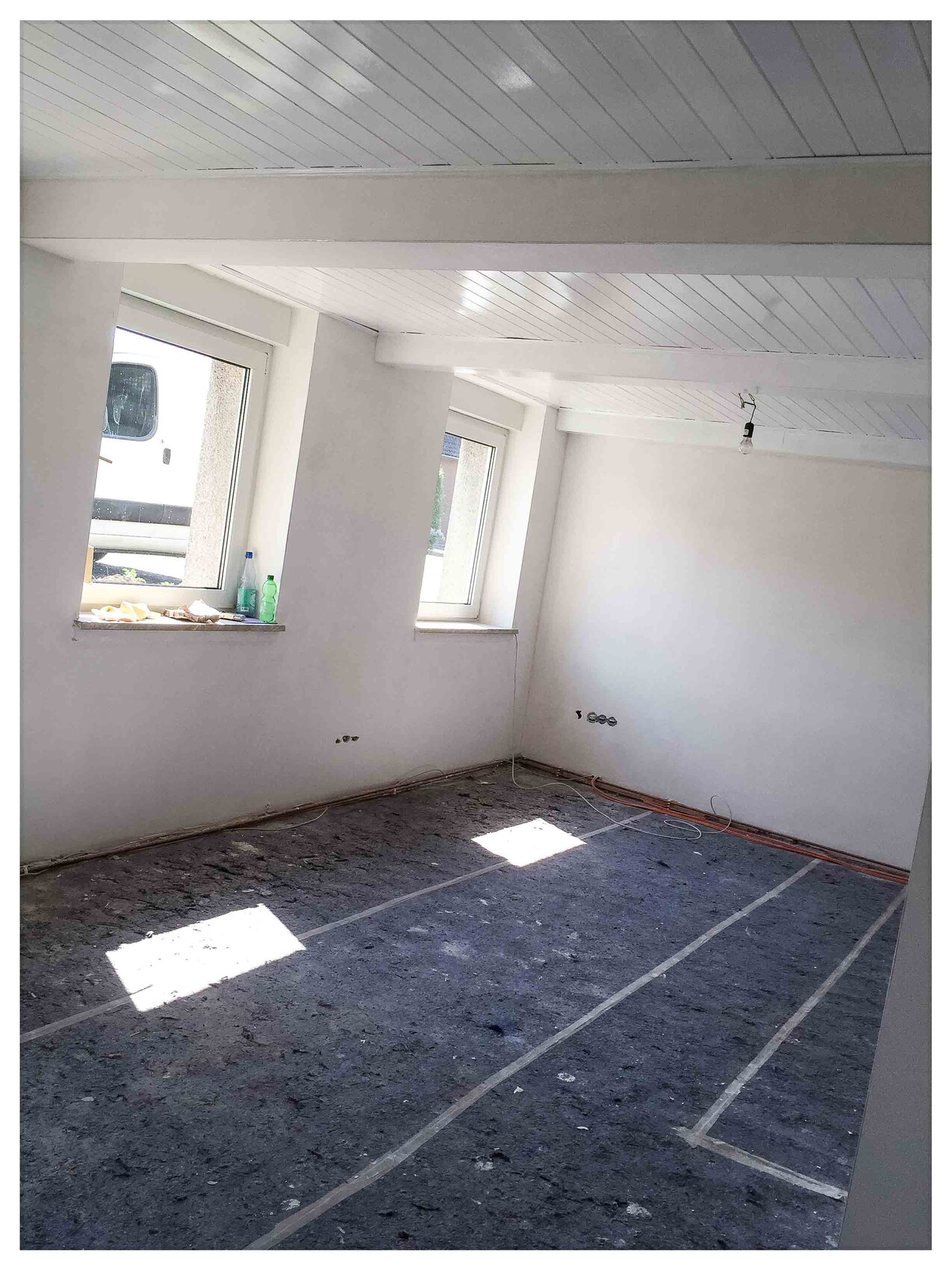 Leerer Renovierungsraum mit weißen Wänden, Deckenverkleidung, Fensterfronten und Kabelresten.