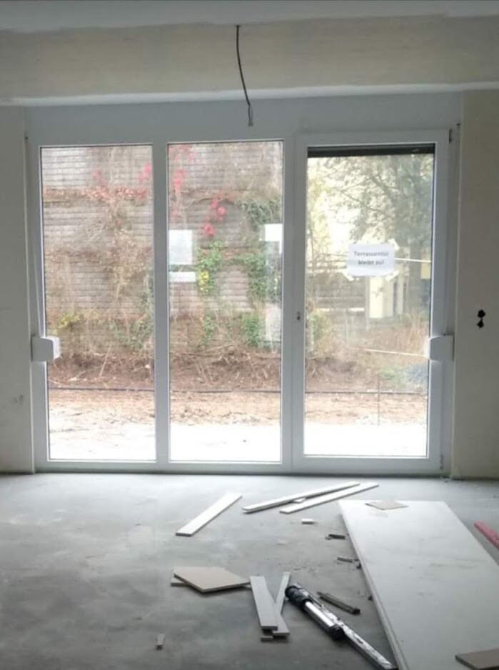 Unfertiger Innenraum mit großer Glas-Schiebetür; Holzreste und Werkzeug auf dem Boden