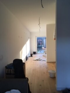Langer heller Innenraum unter Renovierung mit Holzboden, weißen Wänden und Kabeln an der Decke.