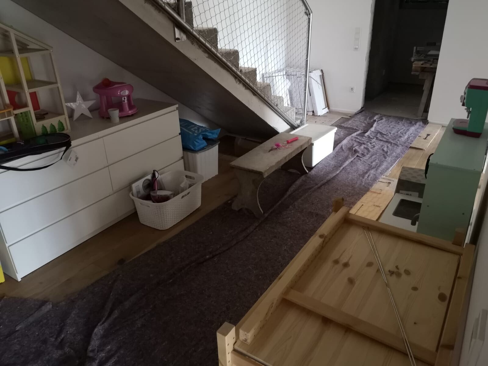 Raum unter Treppe mit weißen Schubladen, Spielzeug und langem Teppich.