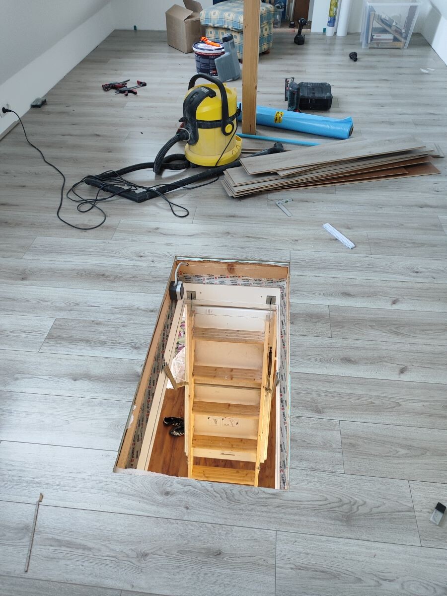 Offene Bodentreppe mit Holzstufen ins Kellergeschoss; Renovierungswerkzeuge und Staubsauger im Raum.