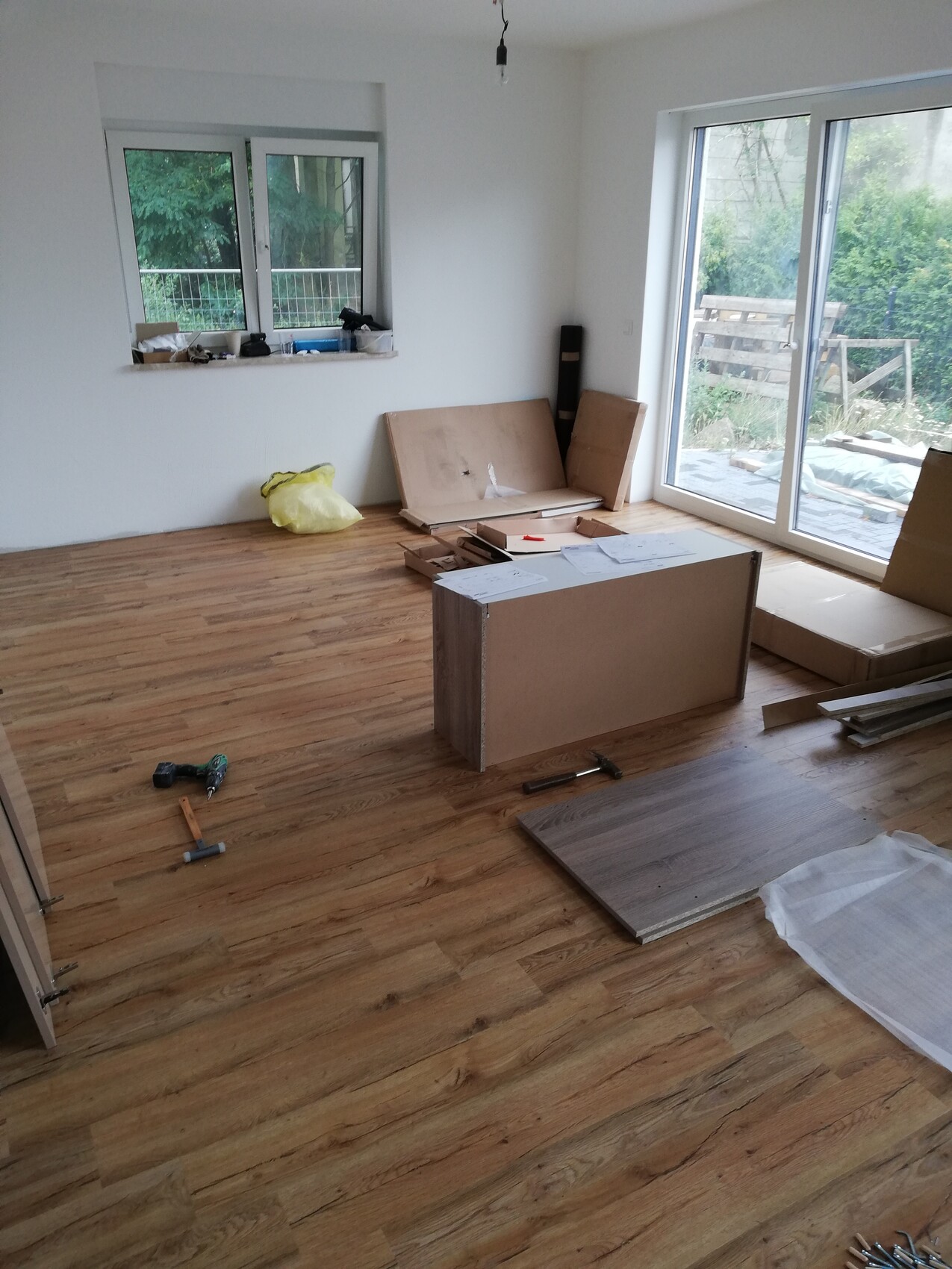 Renovierungsraum mit Holzfußboden, Werkzeugen, Karton und Glasfenstern zur Terrasse.