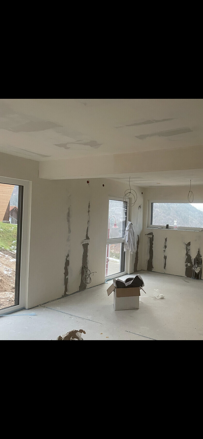 Rohbauzimmer mit freigelegten Wandfugen, losen Kabeln, großen Fenstern und Kartonboxen