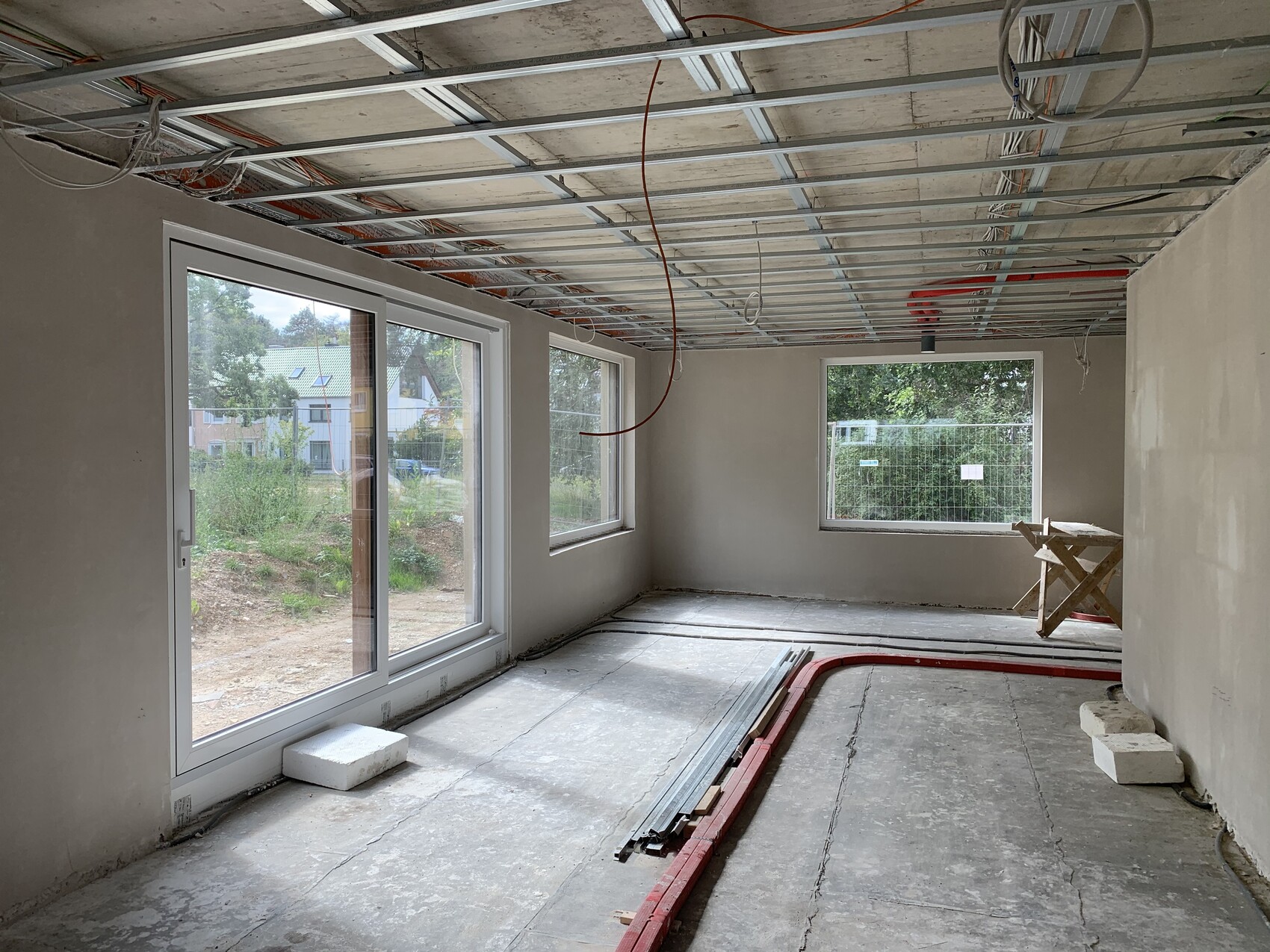 Innenraum unter Bau mit Deckenunterkonstruktion, Rohbauwänden und großen Fenstern.