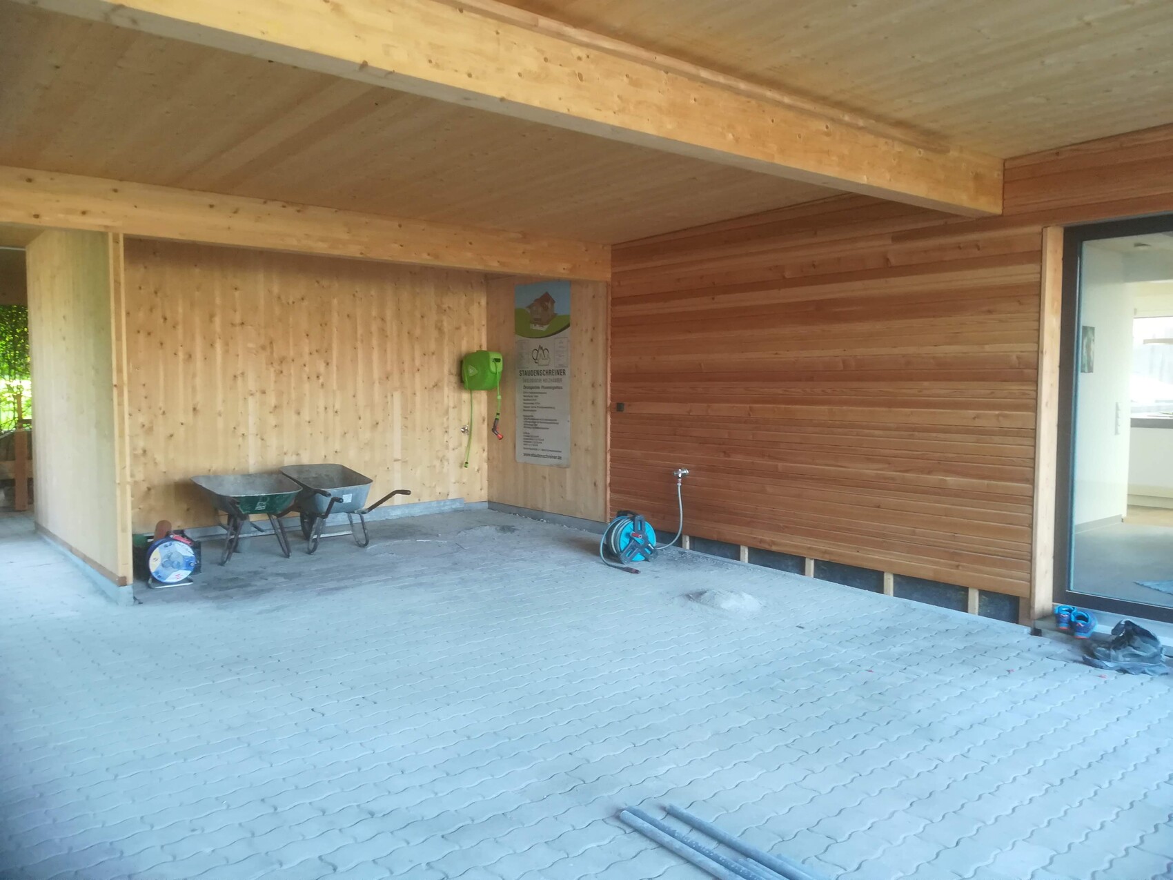 Offener Baubereich mit Holzwänden, zwei Schubkarren, Schlauchrolle und Infotafel.