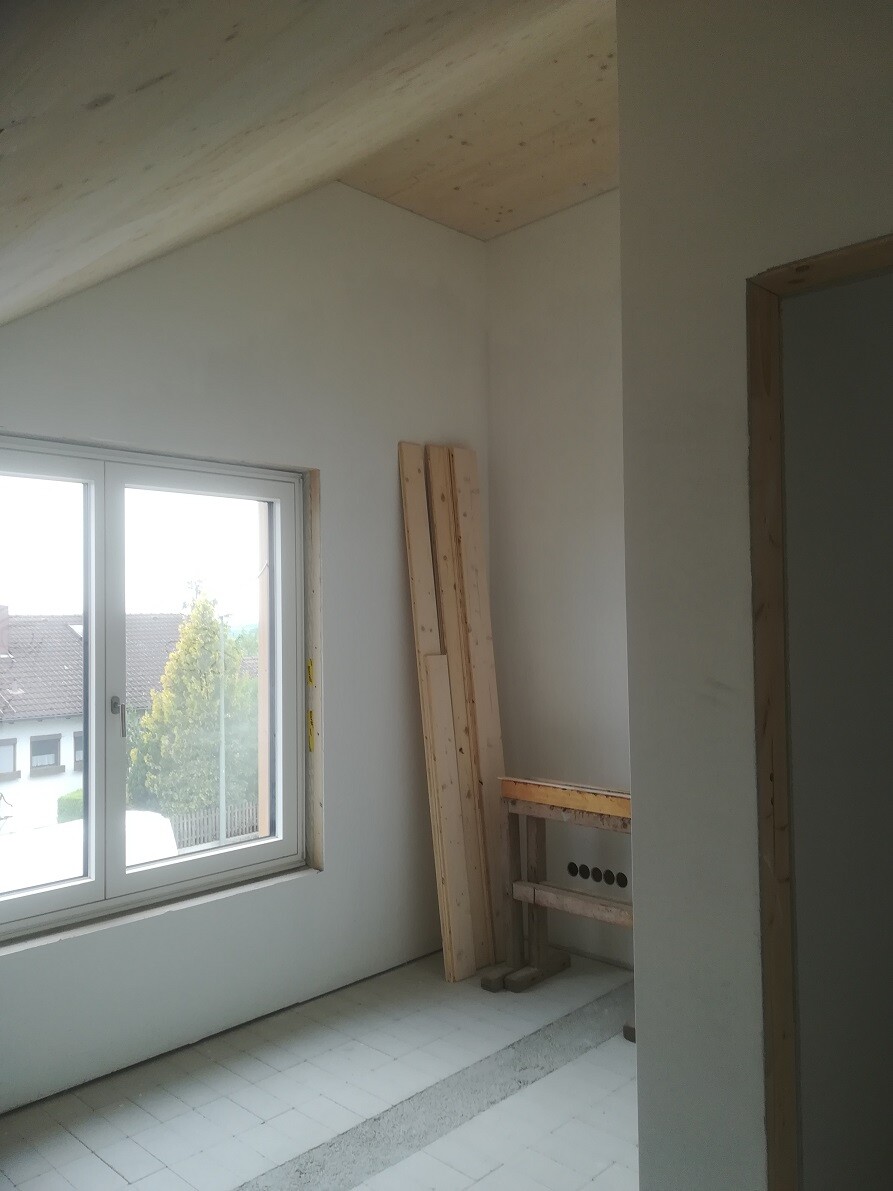 Unfertiges Zimmer mit Fenster, Holzlatten, Werkbank und Bauarbeiten.
