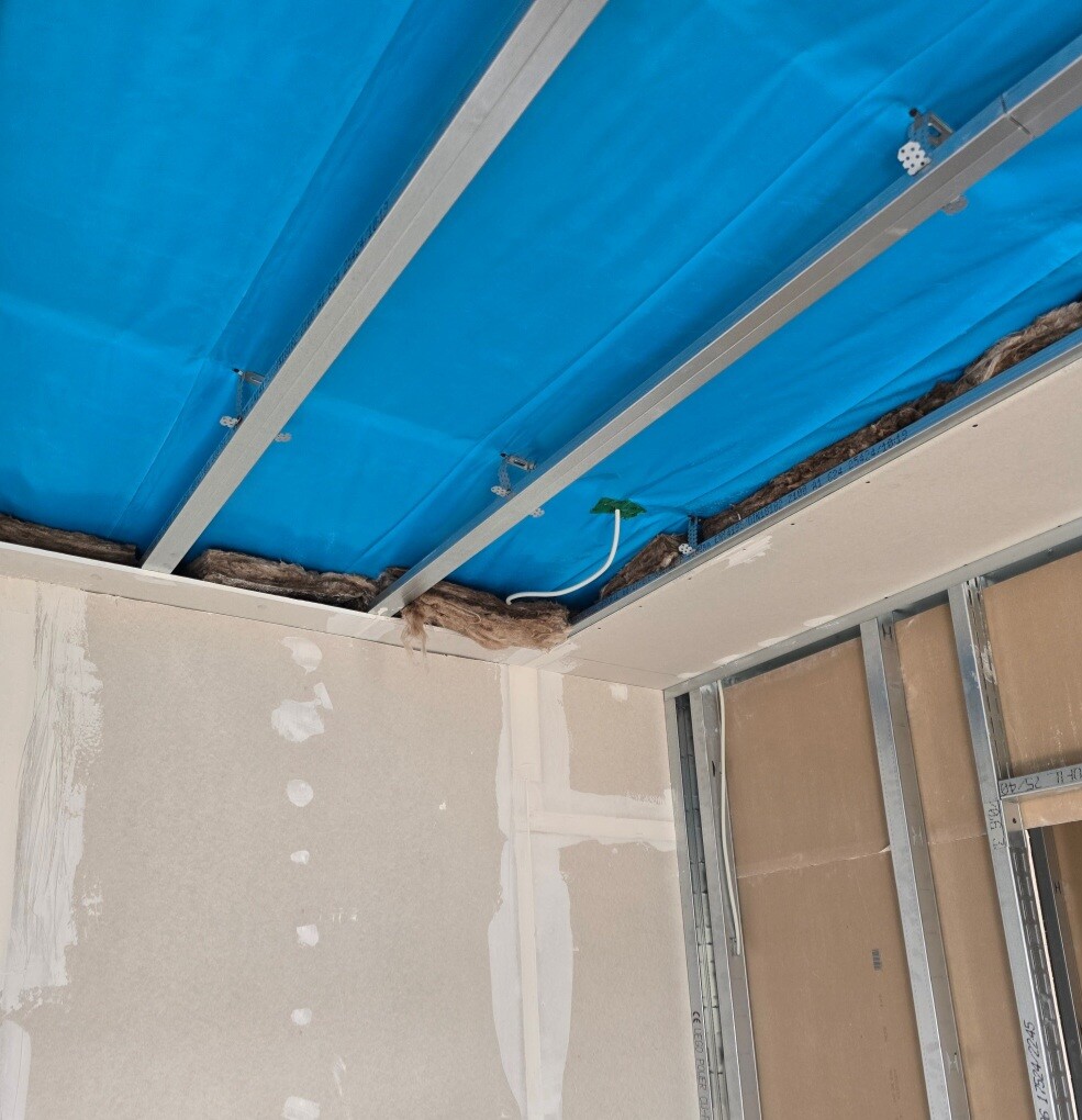 Unfertiger Innenraum mit blauer Abdeckfolie an der Decke, Metallträgern und Kabeln.