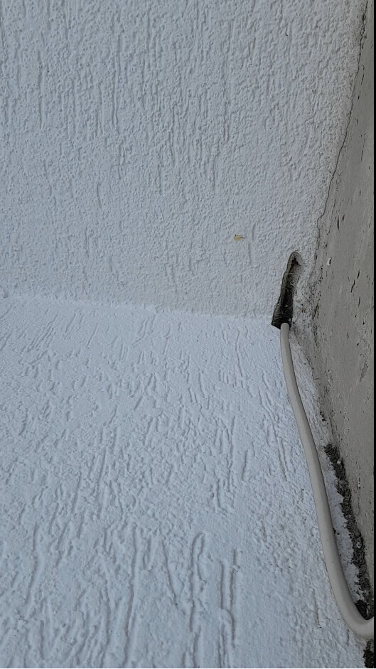 Weiße, strukturierte Wand an einer Ecke; ein weißes Kabel kommt aus einem Wandloch.