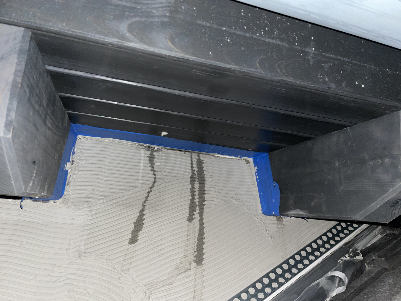 Innenausbau Detail: schwarze Stahlträger, blaues Malerband und verputzter Bodenbereich