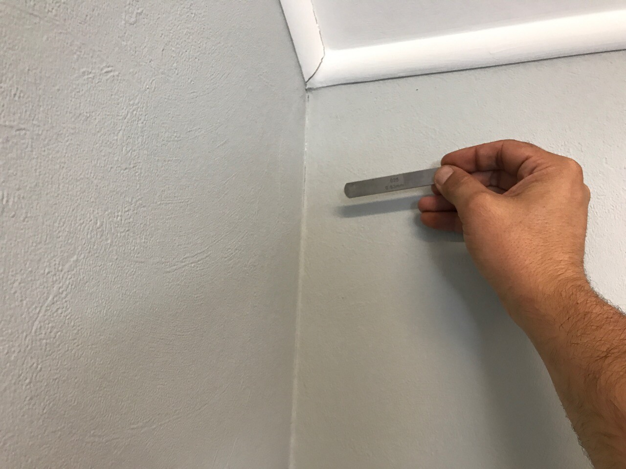 Hand hält eine Metallleiste an eine Wand-Ecke zum Innenausbau messen