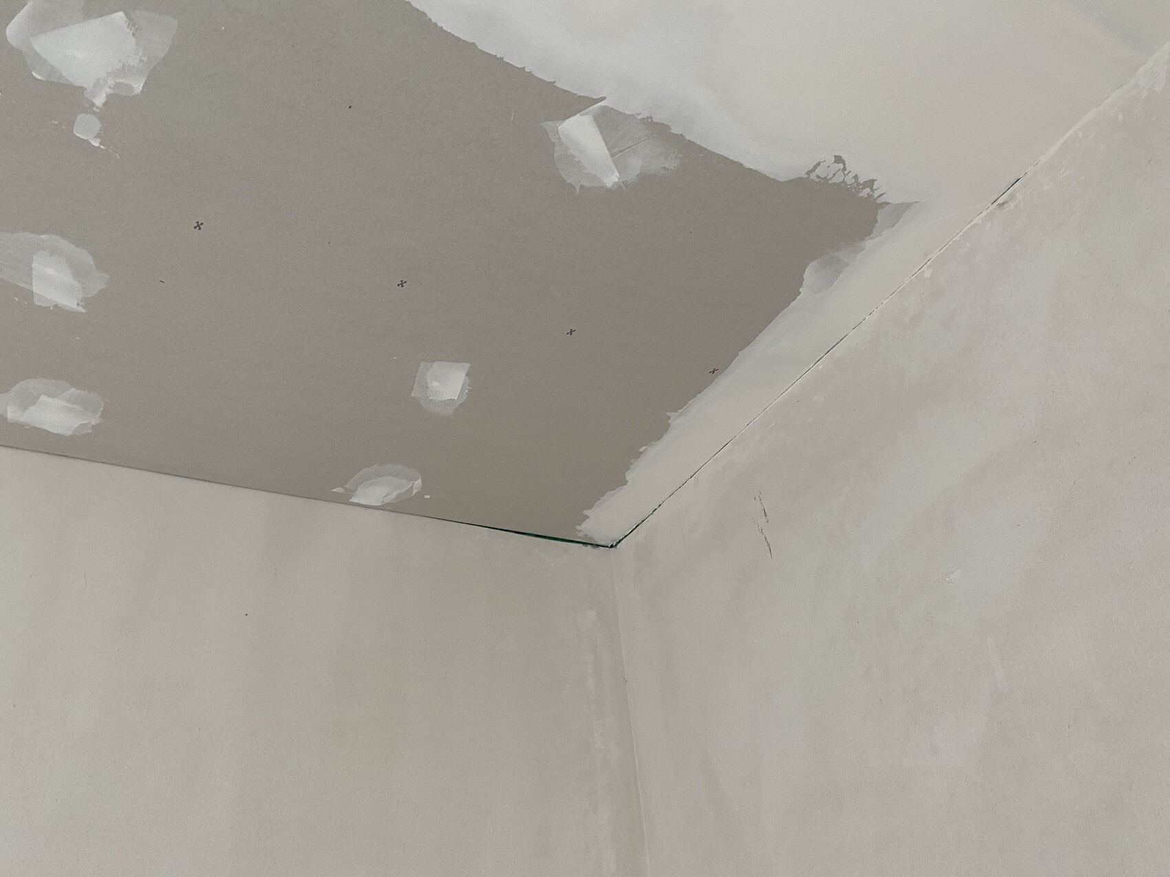 Unfertige Decken- und Wandfläche mit Spachtelarbeiten und Schraubenlöchern in der Ecke.